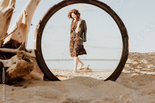 Smilling woman on a sunny beach in dress holding her jacket with her hands  and walking in the reflection of the mirror. happy lifetime