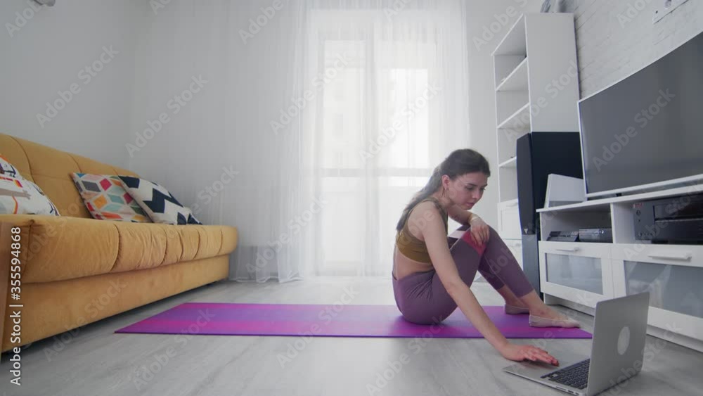 Young beautiful woman stands in bridge pose and spread legs with resistance band with help of his instructor online on laptop at home Young beautiful woman stands in bridge pose and spread legs with resistance band with help of his instructor online on laptop at home