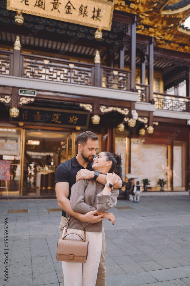 newlywed couple showing affection in Shanghai near Yuyuan. Couple take a break for some hugs while visiting China. husband and wife holding hands on the street by a market and pagoda