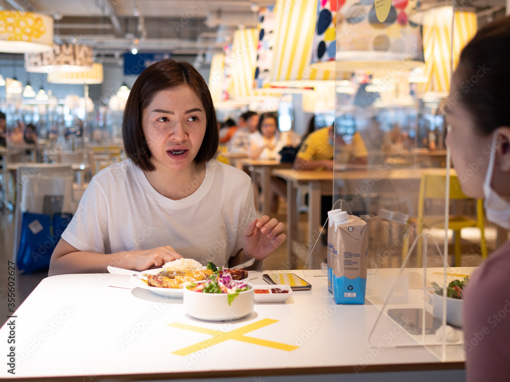 Asian woman sitting separated in restaurant eating food with table shield plastic partition to protect infection from coronavirus covid-19