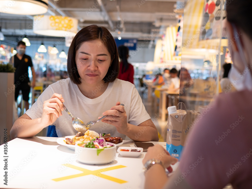 Asian woman sitting separated in restaurant eating food with table shield plastic partition to protect infection from coronavirus covid-19