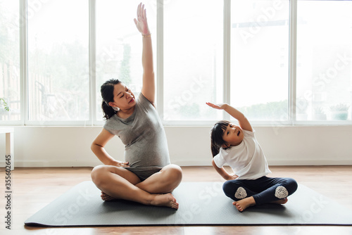 An Asian pregnant woman and child are doing yoga