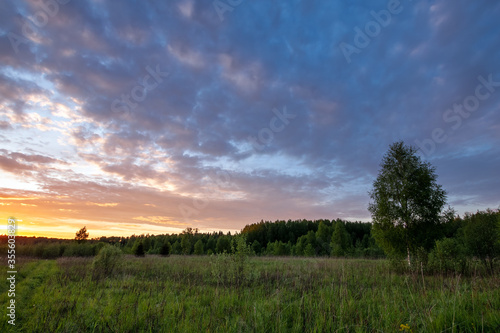 Landscape of sanset of summer meadow under clouds on blue sky