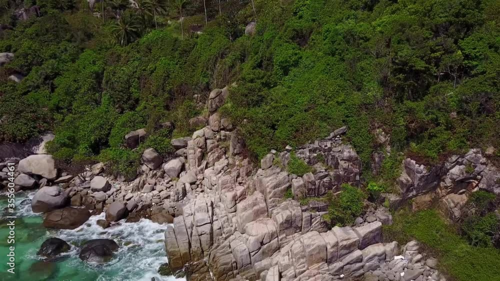 Rocks overgrown with tropical rainforest. Pan-ramming from top to bottom. Below the waves lapping on the rocks. Koh Tao. Thailand Rocks overgrown with tropical rainforest. Pan-ramming from top to bottom. Below the waves lapping on the rocks. Koh Tao. Thailand