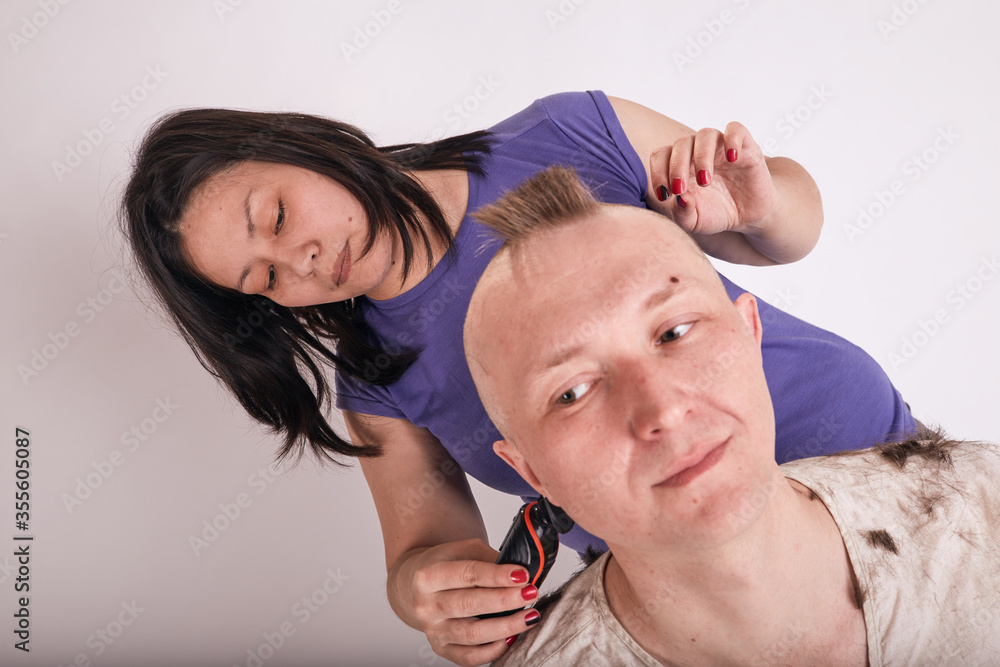 Fototapeta premium Woman doing haircut for man at home while Covid-19 quarantine. Self isolation family lifestyle.