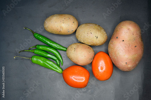 close up of potatoes and tomatoes with green chillies on black background, green chillies and tomatos with patatos on black table, Selective focus photo