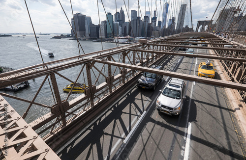 Cars speeding in sun on Brooklyn Bridge with skyline, Manhattan. One of the most iconic bridges in the world, a must see attraction when visiting New York