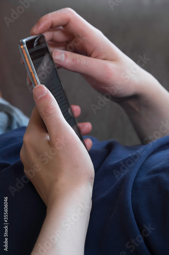Man lying on the couch and reading messages on his smartphone. Vertical photo