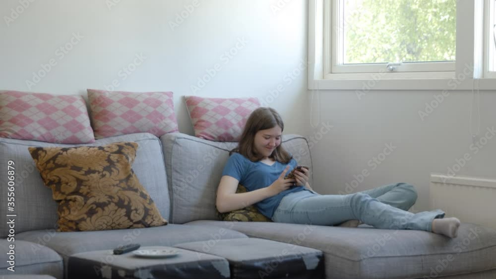 A teenage girl scrolling on her phone and laughing on a sofa. A teenage girl scrolling on her phone and laughing on a sofa.