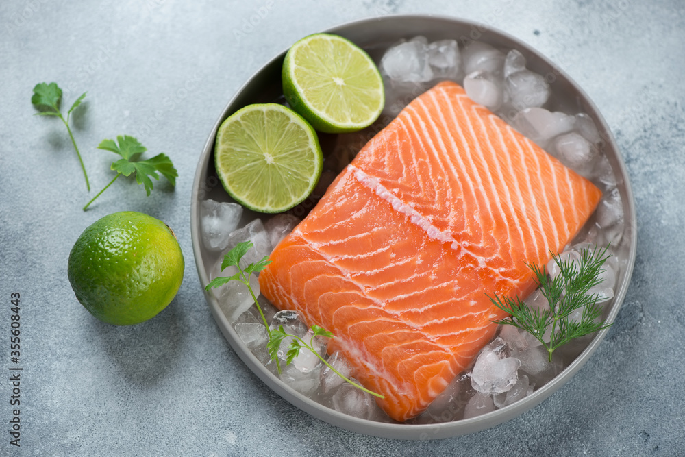 Round grey plate with raw iced salmon fillet and lime, elevated view on a light-blue stone background Round grey plate with raw iced salmon fillet and lime, elevated view on a light-blue stone background