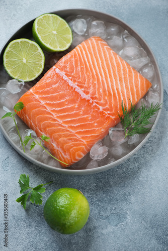 Raw fresh salmon fillet on ice with limes, parsley and dill, studio shot on a light-blue stone background, elevated view