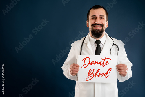 Male doctor with stethoscope in medical uniform holding a white paper photo