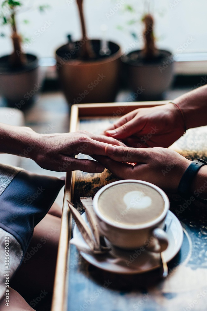 The couple in the cafe holds hands gently. A cup of coffee.