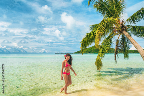 Luxury beach Tahiti Bora Bora bikini woman swimming in paradise getaway vacation. Beautiful Asian swimsuit model relaxing walking in turquoise ocean water in secluded island.