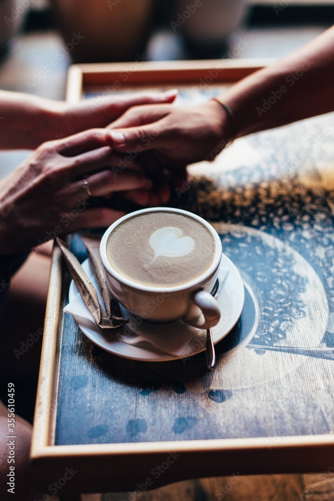 The couple in the cafe holds hands gently. A cup of coffee.