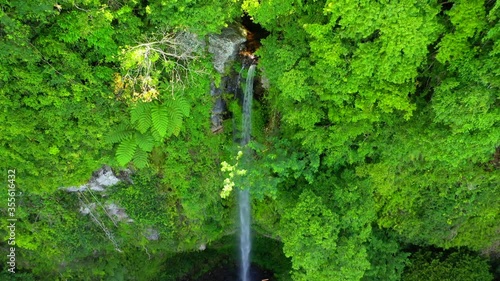 Katibawasan Falls tall waterfall in lush rainforest, tilt down overhead aerial photo