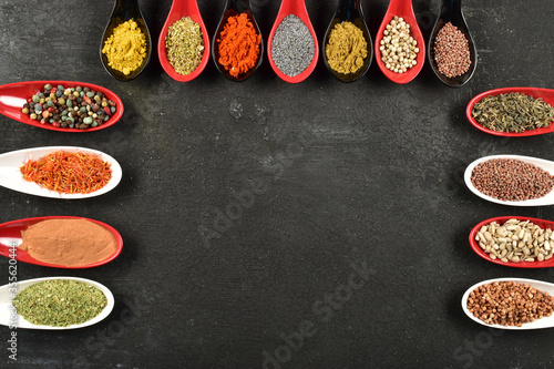 Fototapeta Naklejka Na Ścianę i Meble -  Top view of different kinds of colorful spices in spoons on black stone surface. Blank copy space for message.