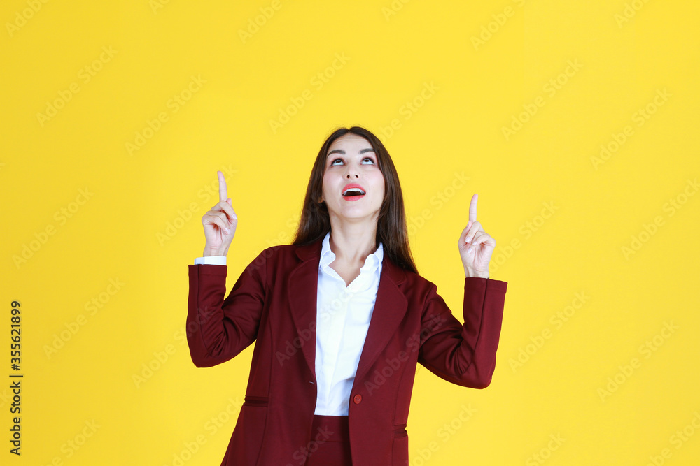 Smart Caucasian woman in red suit smiling and her fingers Pointing top for present isolated on yellow background. Smart Caucasian woman in red suit smiling and her fingers Pointing top for present isolated on yellow background.