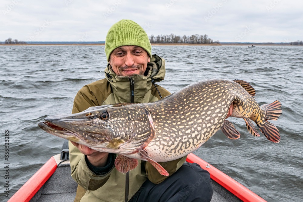 Success pike fishing. Happy fisherman with big fish trophy at boat Success pike fishing. Happy fisherman with big fish trophy at boat