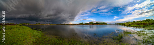 Amazing landscape of nature before thunder storm. Dark clouds cover blue sky at wild river. Incredible weather panorama