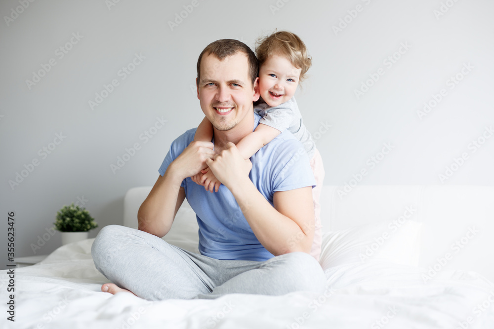 family, love and father's day concept - portrait of happy young father and his cute little daughter sitting and hugging on bed