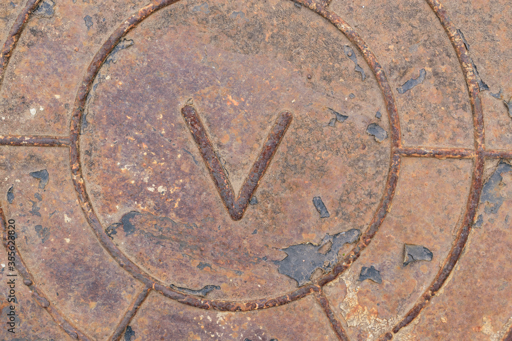 Old metal surface with latin letter V. Rust, scratches, remains of black leather. Concept of word Victory, military shield.