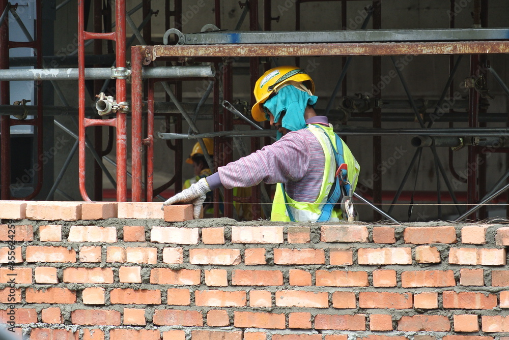 Bricklayer lay clay bricks to form building walls at the construction site. 
