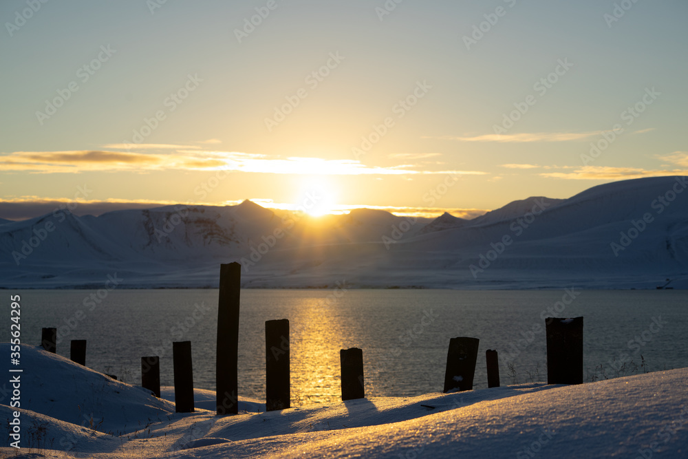 Sunset over a snowy landscape with wooden poles