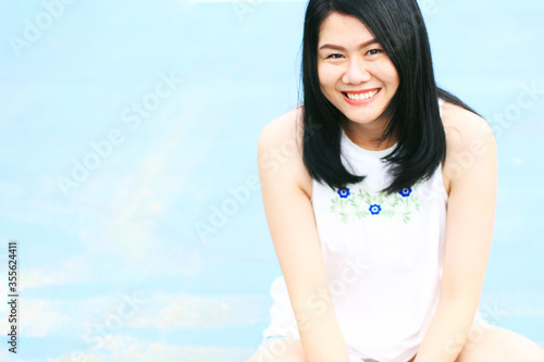 Beautiful asian woman in white dress smiling on blue concrete floor. Thai girl enjoy on holiday concept.