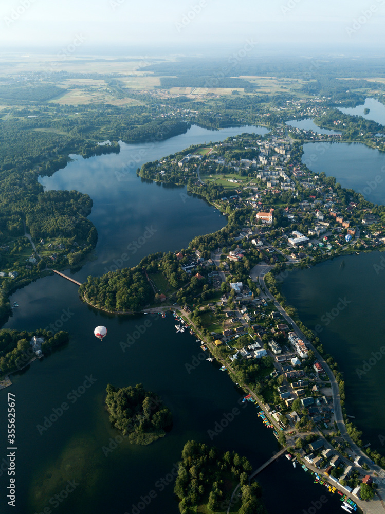 Aerial view of Trakai small town, green island in lake Galve. Rural landscape. Houses, buildings on island, bridge. Balloon flying over city. Clouds reflected in water. Lithuania Europe