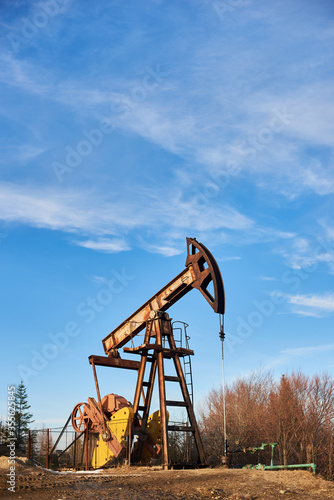 Obraz na plátně Vertical snapshot of pump jack against blue sky on beautiful sunny day, situated in mountainous region, copy space