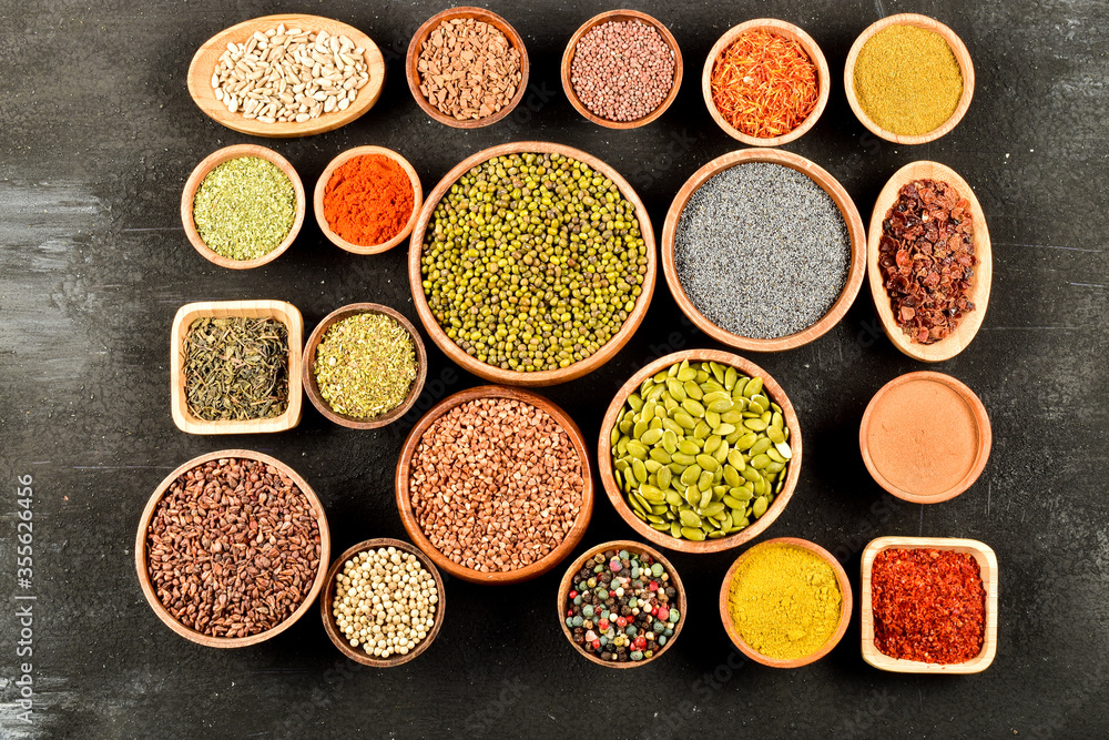 Top view of different kinds of colorful spices in wooden bowls on black stone surface.