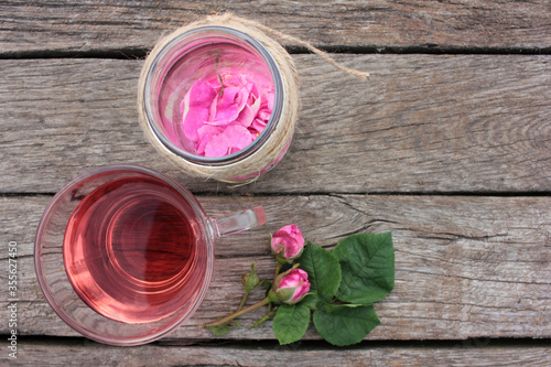 Tea rose herbal tea in a glass cup with pink buds and flowers on a rustic wooden table. Summer tea party outdoors

