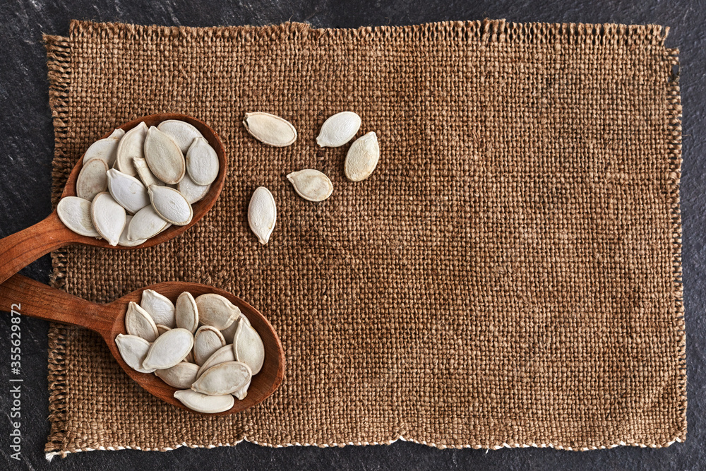 Pumpkin seeds and a wooden spoon with canvas on a dark table. Copy space.