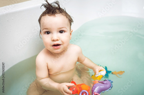 Cute happy little boy washing and playing in bathroom with colorful plastic toys. child's hygiene, healthy skin and body, happy lifestyle, carefree childhood concept