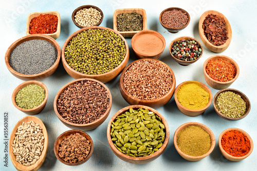 Top view of different kinds of colorful spices in wooden bowls on white surface.