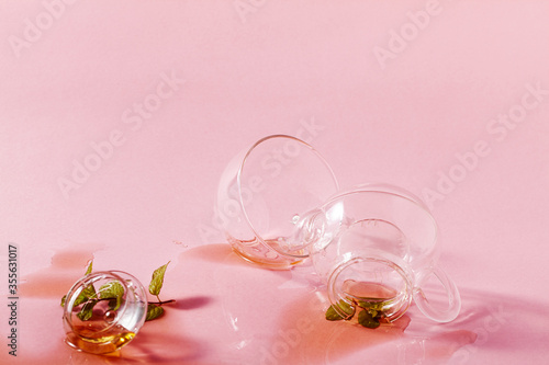 Fototapeta thrown glass teapot and spilled tea on a pink background