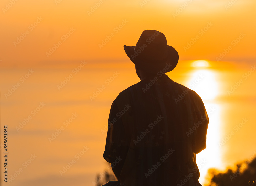 Back silhouette view of a man sitting on the wall and looking at beautiful sunset with clear sky in background.