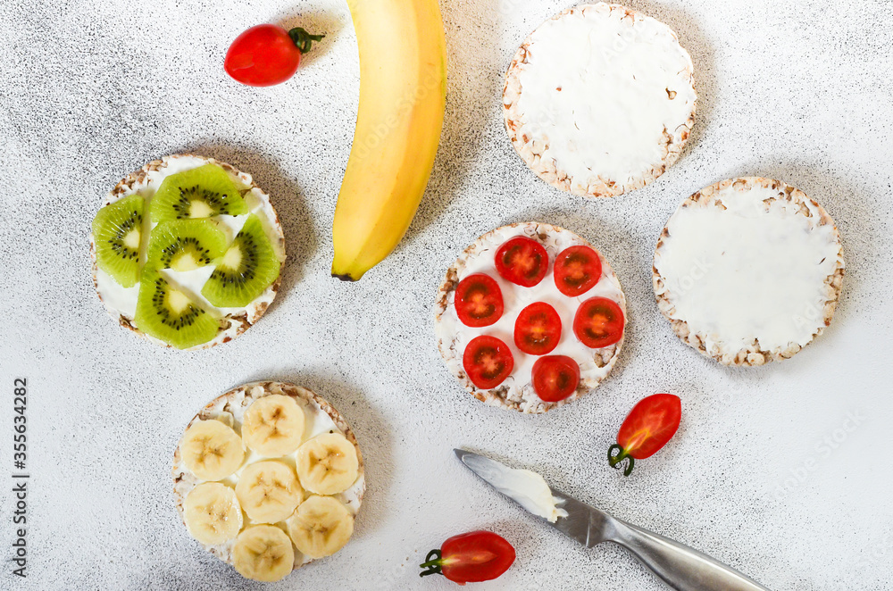 Fototapeta premium Vegetarian food crispbreads with curd cheese, cherry tomato, slices kiwi and banana. A hearty and healthy snack and nutrition in summer lifestyle