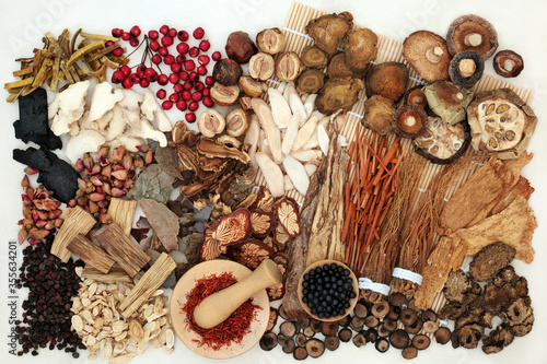 Large selection of traditional Chinese herbs & spices used in herbal medicine with tablets to boost chi levels on a bamboo mat & cream background. Alternative health care concept. Flat lay.