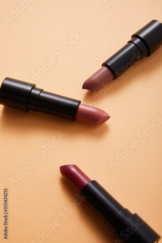 professional face makeup lipsticks on beige background, close view, beauty concept 