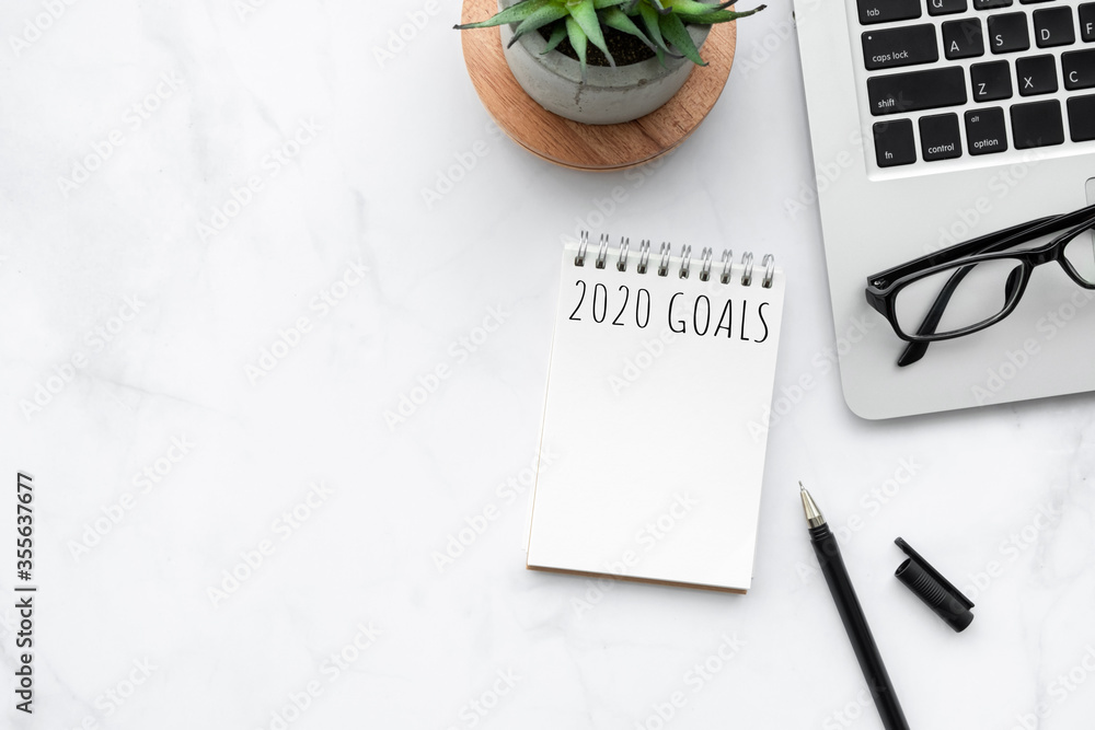 Small blank notebook with 2020 goals text is on top of white marble office desk table with office supplies. New year plan and resolutions concept. - obrazy, fototapety, plakaty 
