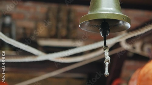 A close-up hand strikes an old ship's bell