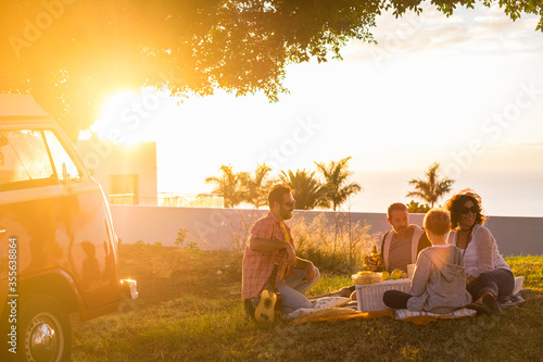 Picnic and outdoor leisure activity for group of adult and young people enjoy friendship together - travel and fun concept with. freinds and sunset - old van in background photo