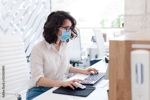 Receptionist wearing medical mask in office. Protection employees on workplace. Young woman working at reception in hotel. Social distancing during quarantine, staff safety.