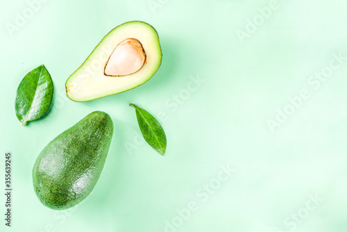Raw organic avocado, whole and sliced avocado on light green background, with green leaves, simple pattern layout, top view copy space