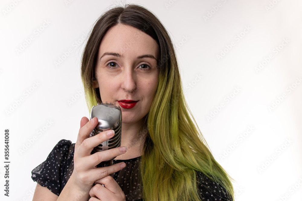 Studio photo of a young attractive woman with brown brunette hair and highlighted green hair, wearing a sexy black dress with red lip stick holding an old retro style microphone on a white background. Studio photo of a young attractive woman with brown brunette hair and highlighted green hair, wearing a sexy black dress with red lip stick holding an old retro style microphone on a white background.