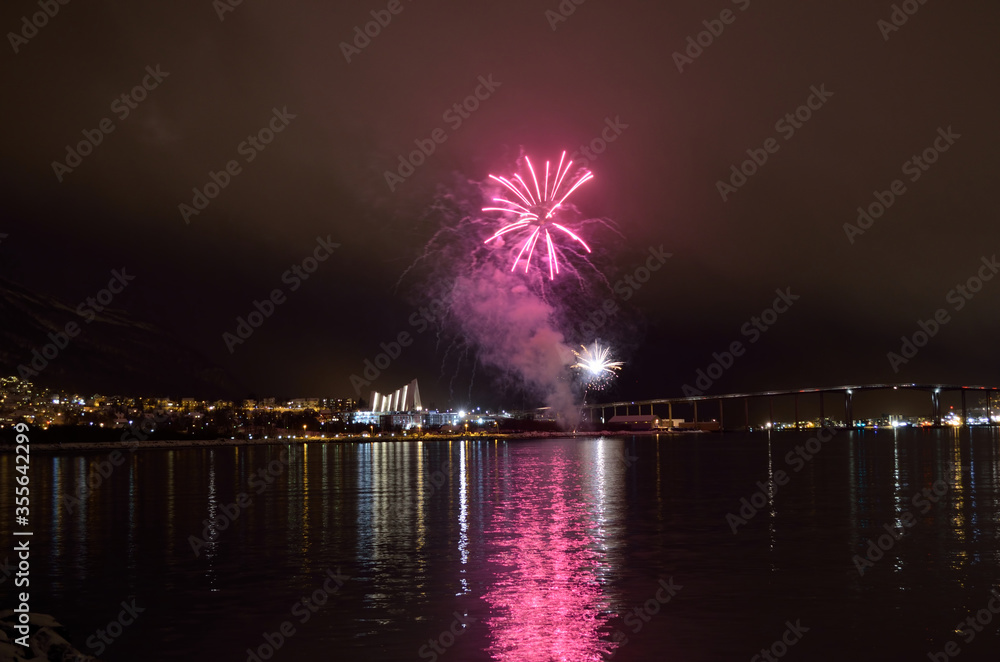 Beautiful firework on night sky in tromsoe city with bridge, cathedral and colorful reflection on the cold fjord water surface on new years eve