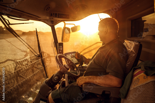 Operator inside a combine harvester at sunset