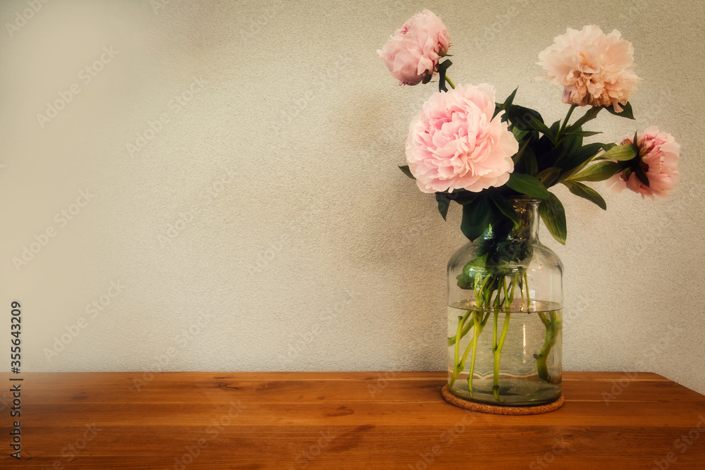 Pink peonies in glass vase on wooden table, romantic design with space for text modern interior Pink peonies in glass vase on wooden table, romantic design with space for text modern interior